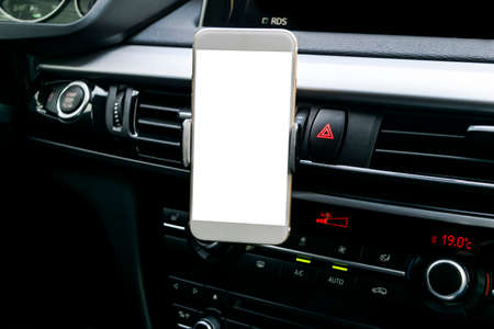 Smartphone in a car use for Navigate or GPS. Driving a car with Smartphone in holder. Mobile phone with isolatede white screen. Blank empty screen. copy space. Empty space for text. modern car interior details.の写真素材