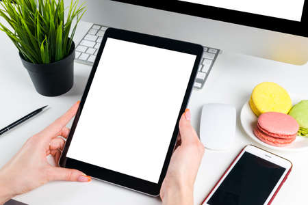 Woman hands holding and using tablet computer with isolated white screen. Business workplace with...