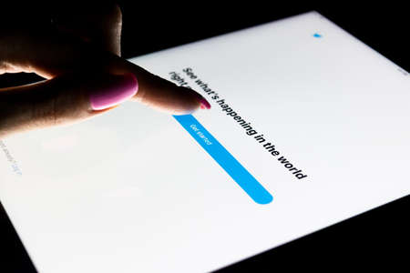 Sankt-Petersburg, Russia, December, 20, 2017:  A woman's hand is touching screen on tablet computer iPad Pro at night Twitter homepage. Twitter.com webpage is online social networking.のeditorial素材