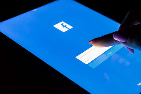 Sankt-Petersburg, Russia, December 20, 2017:  A woman's hand is touching screen on tablet computer iPad Pro at night for Facebook homepage webpage.  Facebook the biggest social network websiteのeditorial素材