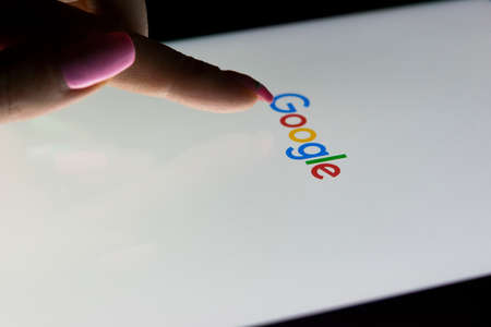 Sankt-Petersburg, Russia, December 21, 2017:  A woman's hand is touching screen on tablet computer iPad Pro at night for searching on Google search homepage. Google is the most popular Internet searchのeditorial素材