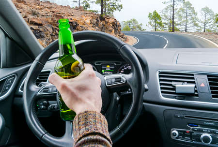 Drunk young man driving a car on the road with a bottle of beer. Don't Drink and drive. Drunk driving under the influence. Driving while intoxicated. Dangerous driving concept.の写真素材
