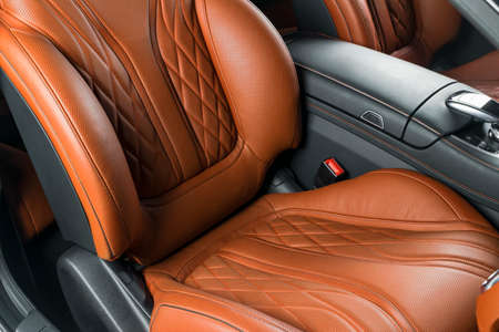 Modern Luxury car inside. Interior of prestige modern car. Comfortable leather red seats. Orange perforated leather cockpit with isolated Black background. Modern car interior detailsの写真素材