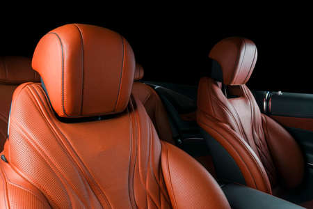 Modern Luxury car inside. Interior of prestige modern car. Comfortable leather red seats. Orange perforated leather cockpit with isolated Black background. Modern car interior detailsの写真素材