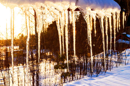 Beautiful icicles shine in sun against blue sky. spring landscape with ice icicles hanging from roof of house. Spring drops icicles dripping. Melting snow icicles on roof.の写真素材