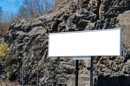 Blank white billboard on city street. In the background street and rocks. Mock up. Poster on street next to roadway. Empty space for text. Copy space. Isolated white screen. Mockup for advertising bannersの写真素材