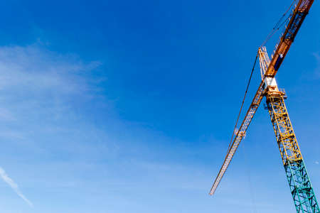 Construction crane tower on blue sky background. Crane and building working progress. Yellow lifting...