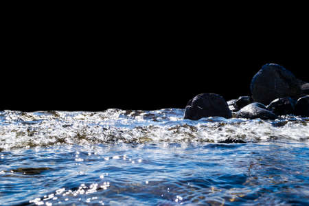 Big windy waves splashing over rocks. Wave splash in the lake on black background. Waves breaking on a stony beach, forming a spray. Water splashes. Water surface textureの写真素材