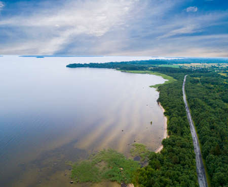 Aerial view of highway. Aerial view of a country road near the lake. Car passing by. Aerial road. Aerial view flying. Captured from above with a drone. Soft lightingの写真素材