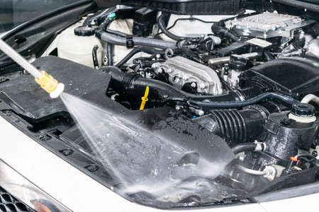 Car detailing. Manual car wash engine with pressurized water. Washing car engine with water nozzle....