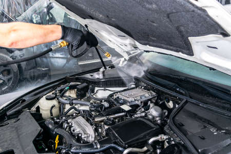 Car detailing. Manual car wash engine with pressurized water. Washing car engine with water nozzle....