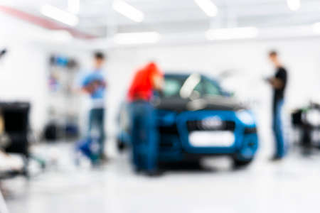 Blurred abstract image of man worker with car in a body shop. Blur car auto service. Car bokeh. Blurred background with car in garage. Vehicle maintenance in auto repair service. Blurry service stationの写真素材