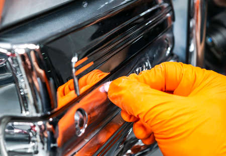 Car polish wax worker hands applying protective tape before polishing. Buffing and polishing car. Car detailing. Man holds a polisher in the hand and polishes the chrome car partの写真素材