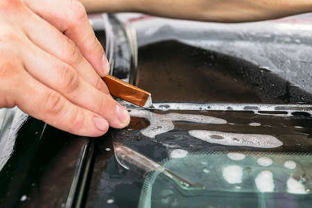 Car wrapping specialist cutting vinyl foil or film on car. Protective film on the car. Applying a protective film to the car with tools for work. Car detailing. Transparent film. Car paint protection. Trimming.の写真素材