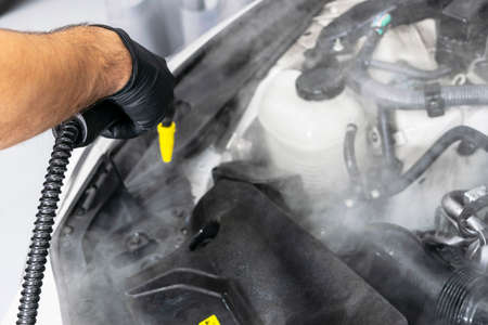 Car detailing. Car washing cleaning engine. Cleaning car engine using hot steam. Hot steam engine washing. Soft lighting. Car wash station worker cleaning vehicle. Car wash conceptの写真素材