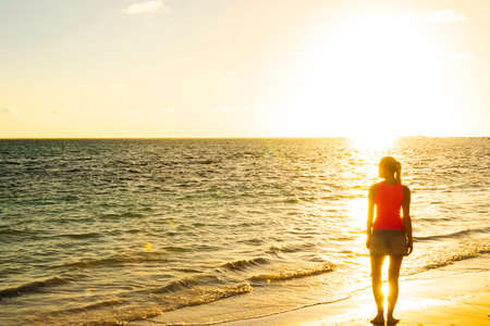 Girl silhouette looking beach sunset standing. Ocean sunset. Tropical beach. Travel concept. Girl looking at the sunset. Model girl silhouette over sunset sky. Swimming and splashing on summer beach over sunset.の写真素材