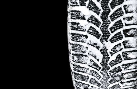 The car tire in the snow close up. Car tracks on the snow. Traces of the car in the snow. Winter tires. Tyres covered with snow at winter road. Isolated on black backgroundの写真素材