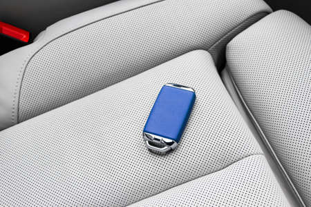Closeup inside vehicle of wireless blue leather key ignition on white leather seat. Wireless start...