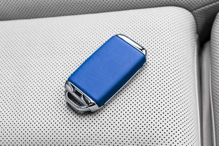 Closeup inside vehicle of wireless blue leather key ignition on white leather seat. Wireless start...