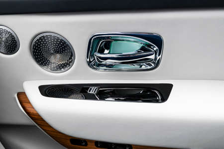 Door handle with power window control buttons of a luxury passenger car. White perforated leather...