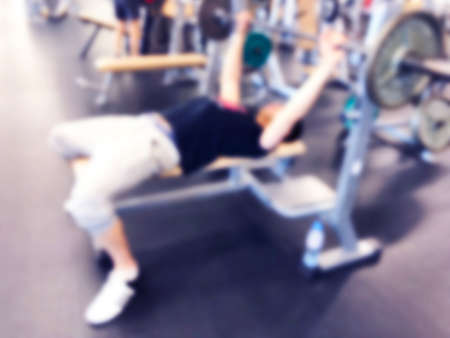 Blurred background with Man Lifting Barbell Row At Gym. Blur Fitness gym with people. Gym equipment...