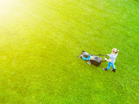 Beautiful girl cuts the lawn. Mowing lawns. Aerial view beautiful woman lawn mower on green grass. Mower grass equipment. Mowing gardener care work tool. Close up view. Aerial lawn mowingの写真素材