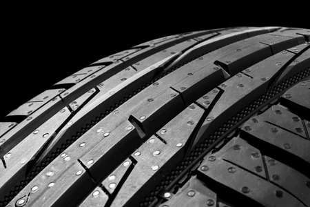 Studio shot of a set of summer car tires on black background. Tire stack background. Car tyre protector close up. Black rubber tire. Brand new car tires. Close up black tyre profile. Car tires in a row. Black and whiteの写真素材