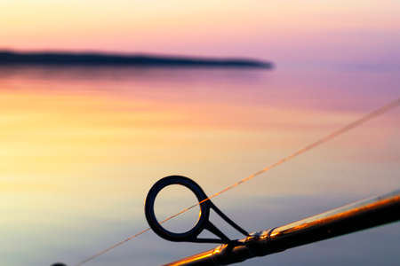 Fishing rod spinning ring with the line close-up. Fishing rod over the crystal still water. Fishing rod rings. Fishing tackle. Fishing spinning reel. Soft lightingの写真素材