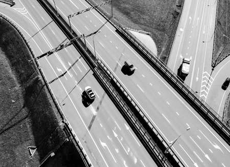 Aerial view of highway and overpass in city. Aerial view of cars crossing interchange overpass. Highway interchange with traffic. Expressway. Road junctions. Car passing by. Black and whiteの写真素材
