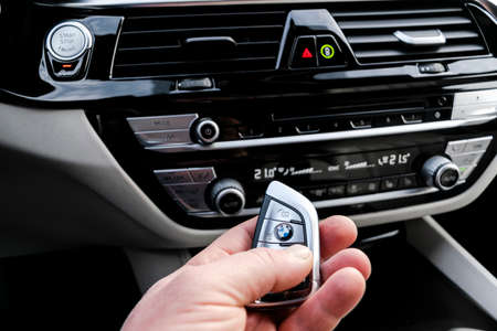 Helsinki, Finland, November 4, 2019: Man's hand holding a wireless BMW 650i 2019 car key in white leather car interior. Modern Car interior details.のeditorial素材