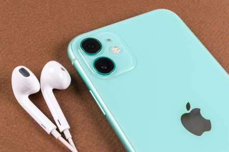 Helsinki, Finland, January 13, 2020: Apple iPhone 11 camera and headphones close up on office desk....