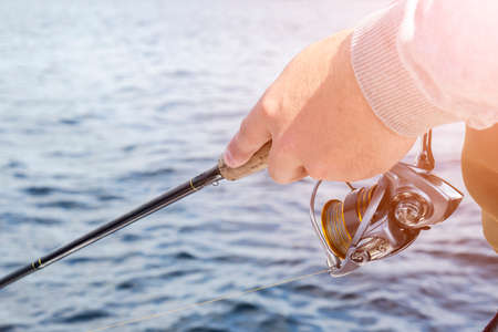 Fishing on the lake. Hands of fisherman with fishing rod and reel. Macro shot. Fishing rod and hands of fisherman over lake water. Spinning rod. Fishing tackleの写真素材