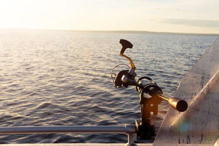Fishing rod spinning with the line close-up. Fishing rod in rod holder in fishing boat due the fishery day at the sunset. Fishing rod rings. Fishing tackle. Fishing spinning reel.の写真素材