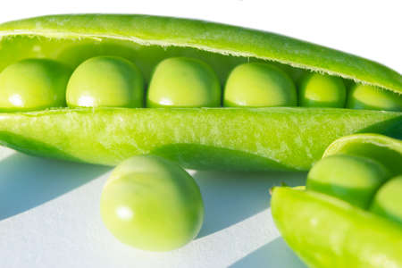 Macro shot fresh green peas with beans isolated on white background. Sweet peas in close up isolated over white with clipping path. Opened pea pods with beans isolatedの写真素材