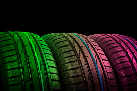 Studio shot of a set of summer car tires in green and pink tones. Tire stack background. Car tyre...