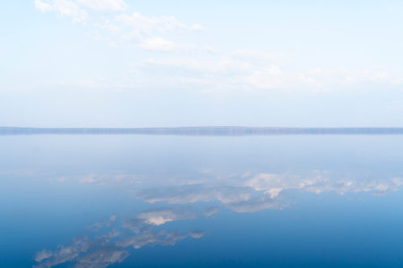Lake surface with calm water. Smooth water surface with cloud reflections and horizon line. Still calm water textrure background.の写真素材
