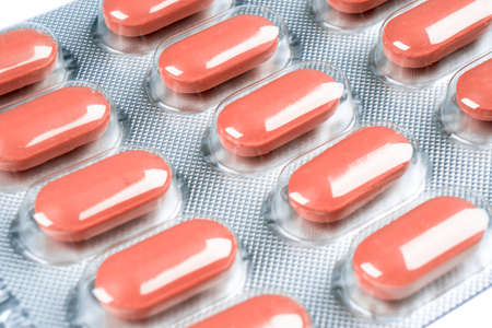 Macro shot pile of red tablets pill in blister packaging isolated on white background. Aluminium foil blister pack. Pharmacy products. Medicine pills and drugs close up. Health care. Pills backgroundの写真素材