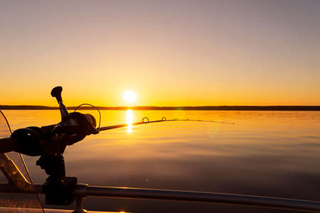 Fishing rod spinning with the line close-up. Fishing rod in rod holder in fishing boat due the fishery day at the sunset. Fishing rod rings. Fishing tackle. Fishing spinning reel.の写真素材