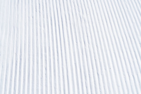 Close up of groomed tracks on a slope in a downhill ski resort. Close-up straight line rows of...