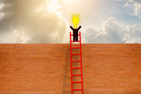 Success concept. man have idea standing on top of ladder over brick wall with Cloud background.の写真素材