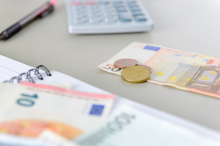 Euro money banknotes and coins counting with calculator, notebook and pen on deskの写真素材