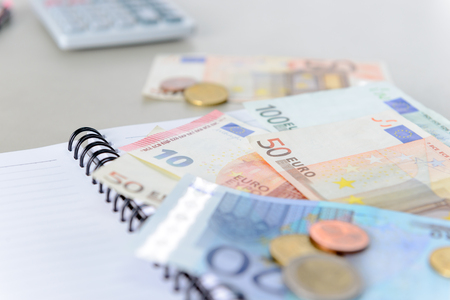 Euro money banknotes and coins counting with calculator, notebook on deskの写真素材