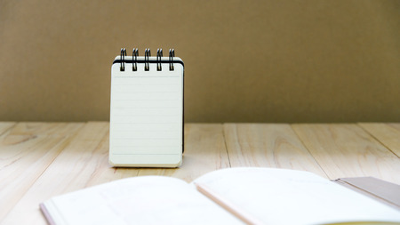 Small note book paper (notepad) stand for writing information with pencil and book on wood table