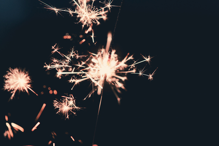 Female hands holding sparkler with night background - bright festive Christmas or New Yearâ€™s...