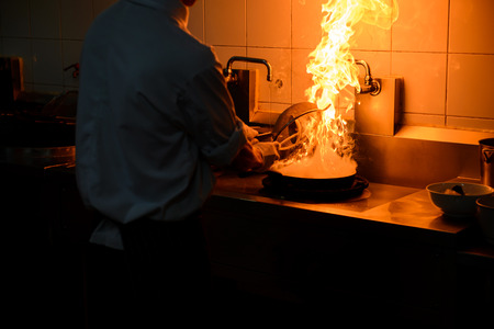 Chef cooking and doing flambe on food in restaurant kitchenの写真素材