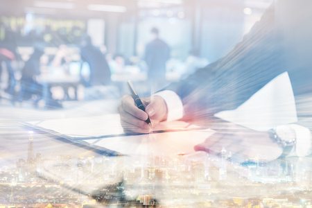 Double exposure of business man signing contract document in office with cityscape and blurred of business meetingの写真素材