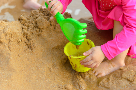 girl playing with shovel toys on the beach in summertime - childhood and summer conceptの写真素材