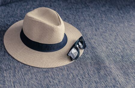 straw hat with black ribbon and sunglasses on sofa wtih free space, vacation travel in summer...