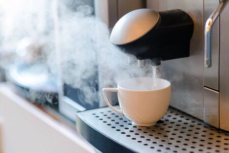 White cup standing on grating of automatic coffee maker machine. Coffee break conceptの写真素材