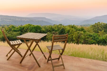 Empty wooden table and chairs on terrace. Beautiful seating with landscape mountains view while...
